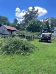 Bobcat excavator near brush pile and barn.